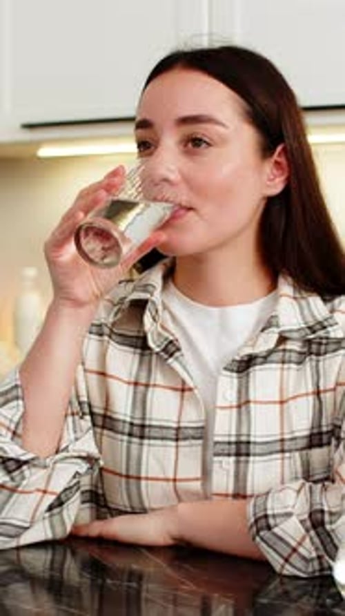 Young Woman Pours Water into Glass at Home