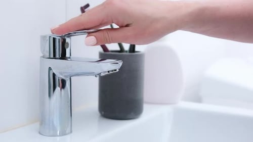 Woman Turns on Faucet in Bathroom Sink