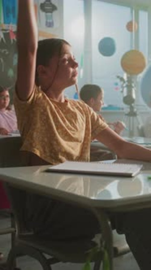 Primary School Children Sitting at the Desks Raising Hands to Give Correct Answer