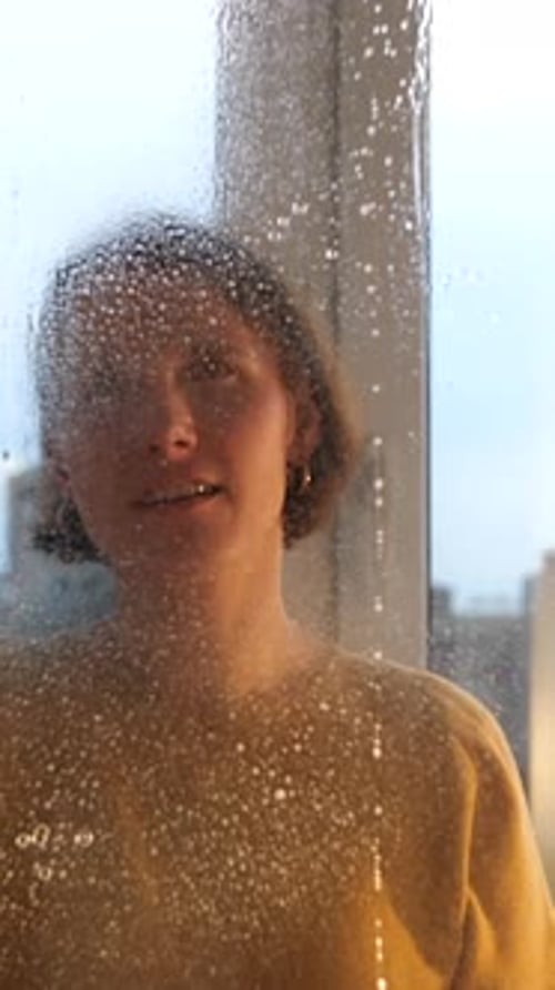 Vertical Young Woman Sprays Detergent Onto a Window and Wipes It Dry with a Rag