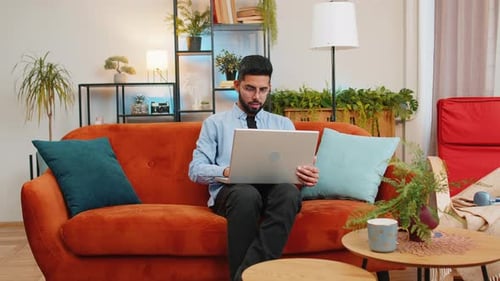 Man Opens Laptop on Couch in Living Room