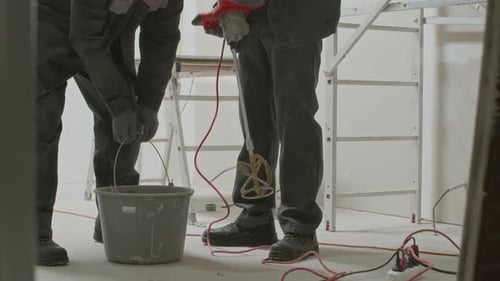 Builders Using Paddle Mixer to Dilute Cement in Bucket on Construction Site