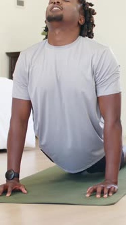 Vídeo vertical: Presionando las palmas, hombre en camiseta gris arqueando la espalda sobre una colchoneta verde para hacer yoga con reloj de pulsera