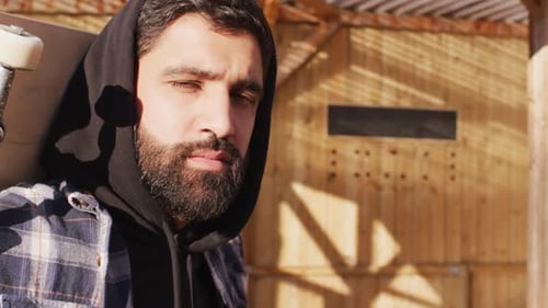 Video of midsection of middle eastern male skateboarder holding skateboard in skate park