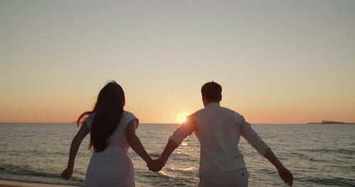 Young Loving Couple Jump on the Beach Together at Sunset