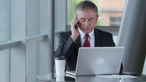 Mature businessman discussing business on cellphone in modern office lobby