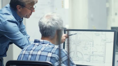 Two Senior Architectural Engineers Working With Building Plan on a Personal Computer. They Actively