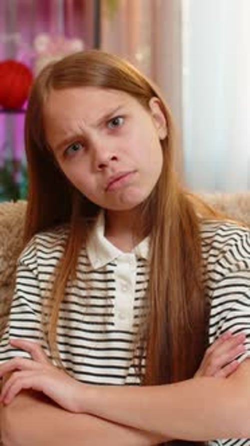 Child Girl Kid Crosses Arms in Anger Sitting on Sofa Expressing Frustration Dissatisfaction at Home