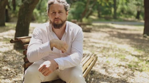Thoughtful Bearded Man Sitting on a Park Bench Pointing Upwards