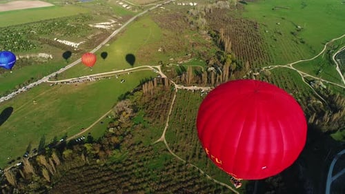 Red Hot Air Balloon Flying Over Green Fields in Cappadocia