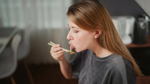 Woman Eating Noodles with Chopsticks in Her Home