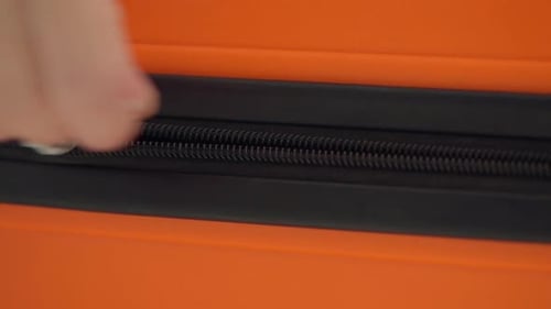 Close View of Hand Closing Zipper on Bright Orange Travel Suitcase