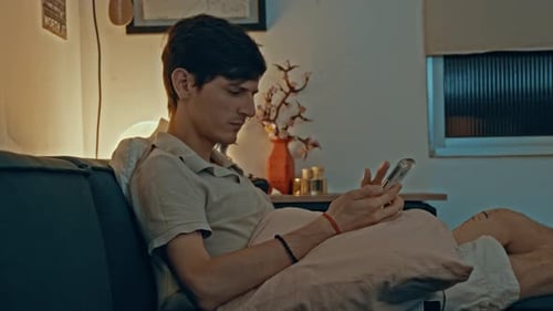 Man Relaxes on Couch, Looking at Phone Indoors