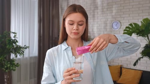 Young Woman Preparing a Refreshing Drink By Pouring Powder Collagen Into a Glass