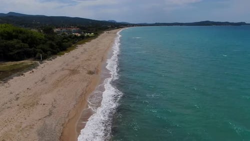 Aerial Drone Follows Person Walking Alone on a Long, Empty Sandy Beach next to Turquoise Sea.