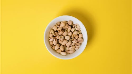 Pistachios in a Bowl on a Bright Yellow Background Stop Motion Video with the Pistachios Nuts