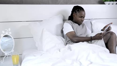 Man Relaxing in Bed Using a Tablet
