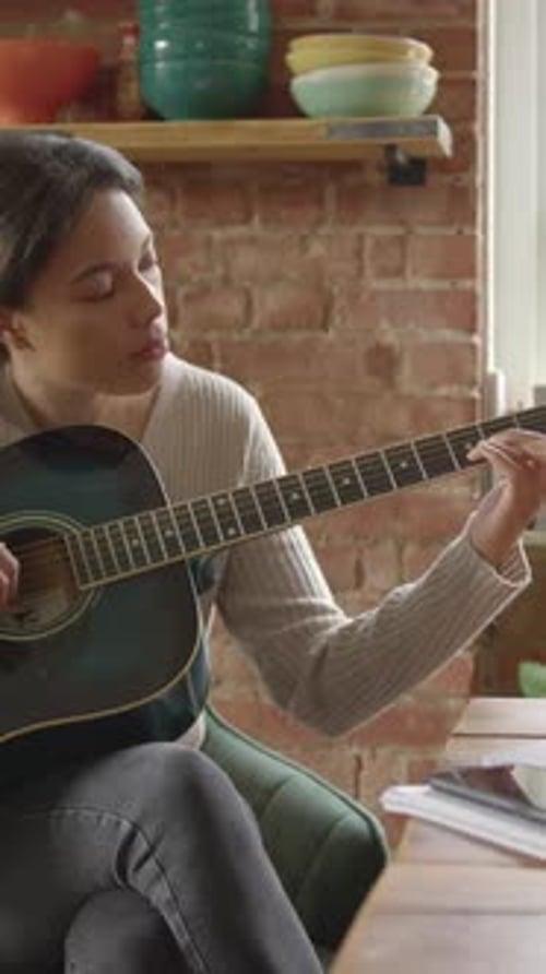 Woman plays acoustic guitar in a casual home setting