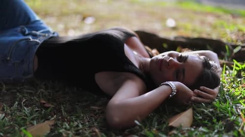 Latina woman lies on grass ground outside carefree