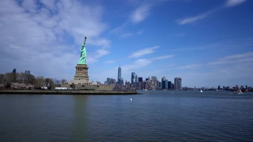 Statue of liberty island with NYC skyline in background across water, wide