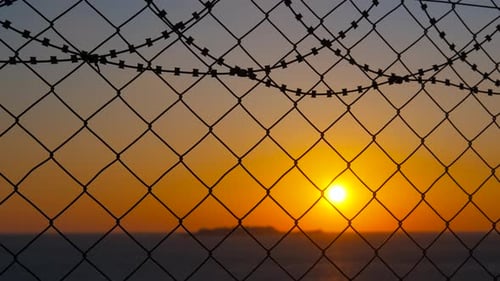 Sunset Through Barbed Wire Fence Over Ocean