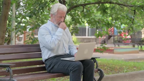 Senior Man Using Laptop in Park and Coughing