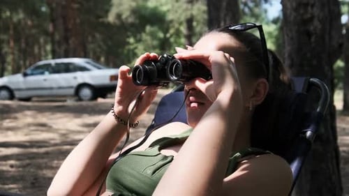 Woman Using Binoculars Reclined in Folding Chair Outdoors