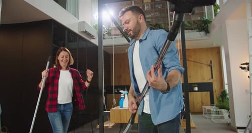 Close Up of Young Funny Couple Having Fun Dancing Singing Using Mop and Vacuum Cleaner Pretending