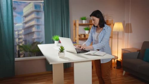 Woman Working at Standing Desk with Laptop and Notebook
