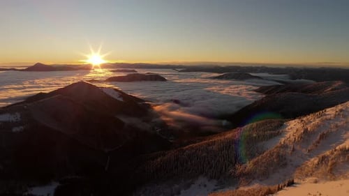 Aerial Sunrise Over Winter Mountains with Sea of Clouds Below and Snowy Forest Ridge in Foreground