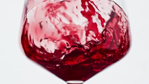 Rotwein formt eine wunderschöne Welle und gießt Wein in ein Weinglas auf weißem Hintergrund