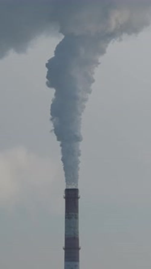 Tall Chimney Emitting Smoke Against Overcast Sky