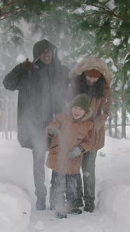 Young Mom, Dad and Son Having Fun Snow Shower in Winter Forest