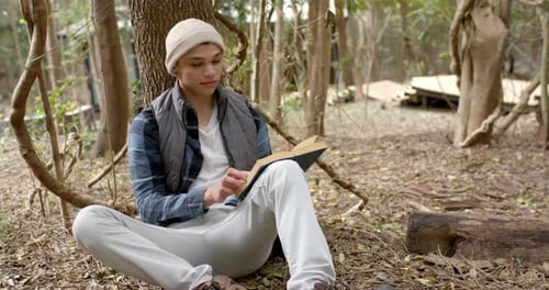 Asiatischer Mann sitzt unter einem Baum und liest ein Buch und genießt die friedliche Umgebung im Freien