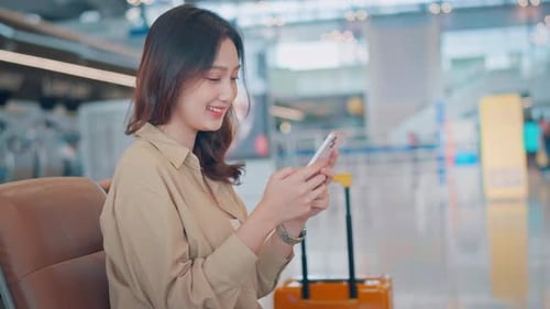 Asian tourist woman using mobile phone and watching watch between waits for flight in Airport
