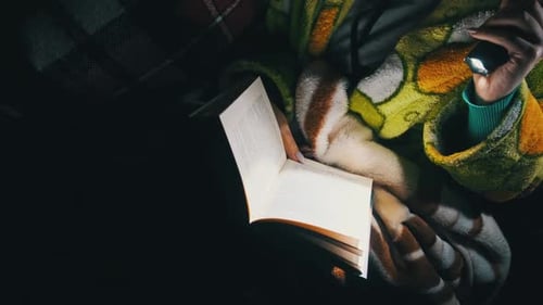 Frau liest ein Buch während eines Stromausfalls im Licht einer Taschenlampe
