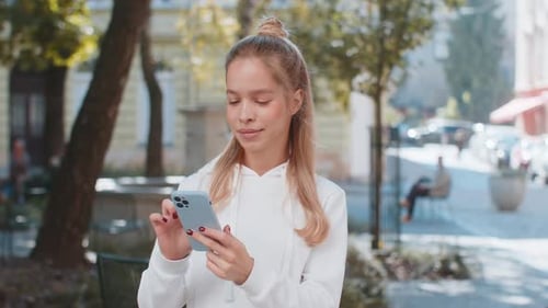 Happy Caucasian Woman Using Smartphone Typing Text Messages Browsing Internet on City Town Street
