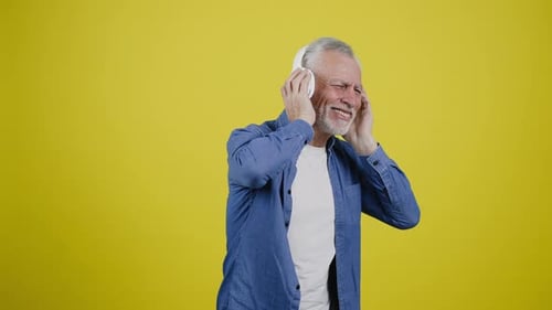 Senior Man Dancing with Headphones Against Yellow Backdrop