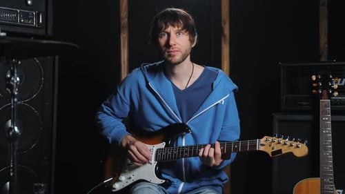 Young Man Recording Guitar Lessons for Students at Music Studio