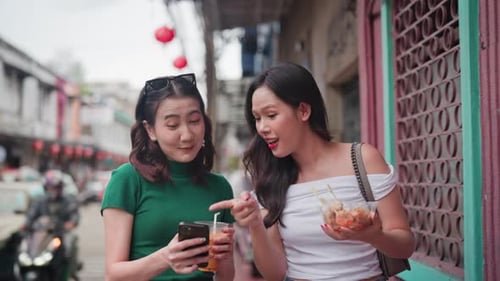 Asian Women Exploring Chinatown Street with Smartphone and Snacks