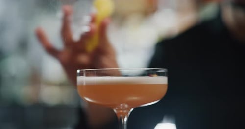Close up of a professional bartender is squeezing a lemon while preparing an alcoholic cocktail wi