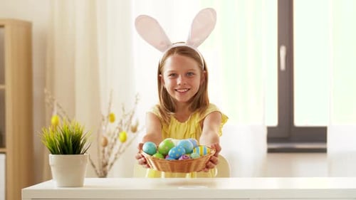 Glückliches Mädchen mit Hasenohren zeigt im Frühling zu Hause ein farbiges Osterei