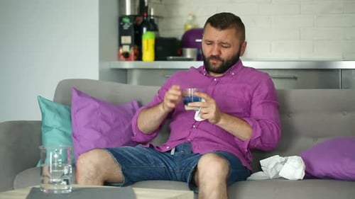 Bearded Man Taking Medicine on Couch at Home