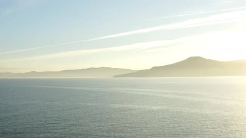 Beautiful aerial drone view sunset over the ocean and mountains on the horizon.