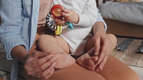 Frau hält barfuß Baby in der Hand und berührt sanft ihre rosafarbenen Füße