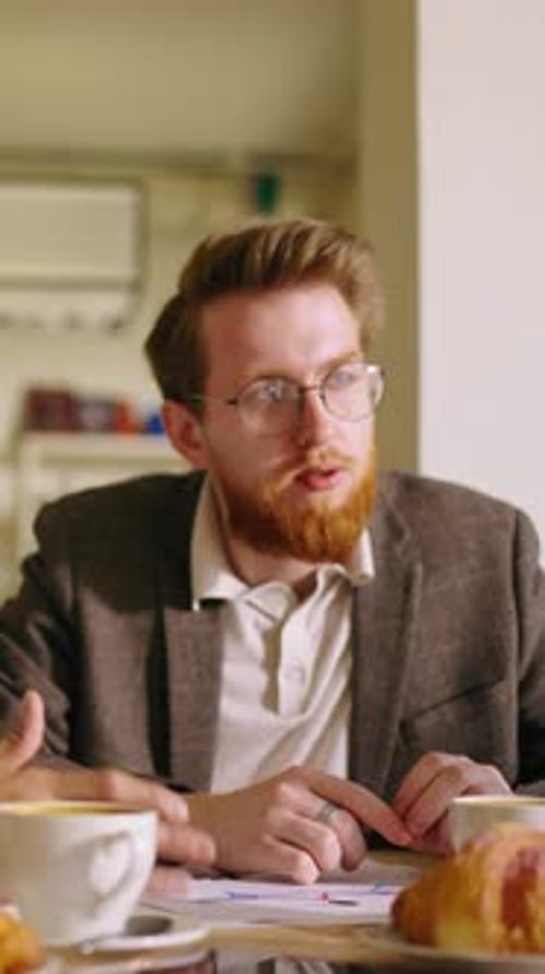 Two Young Men Engaged in Focused Conversation at a Cozy Cafe Table Discussing Documents and Ideas