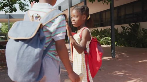 Video of happy african american boy and girl with schoolbags high fiving outside school