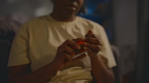 Person Opens Bottle of Pills in Dark Room