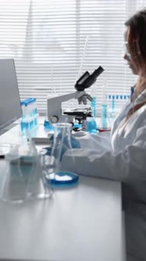 A Female Scientist Conducting Experiments in a Laboratory Using a Microscope and Test Tubes for Her