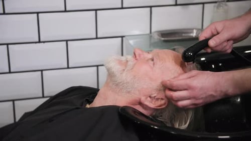 Barber Washing Senior Man's Grey Hair in Salon